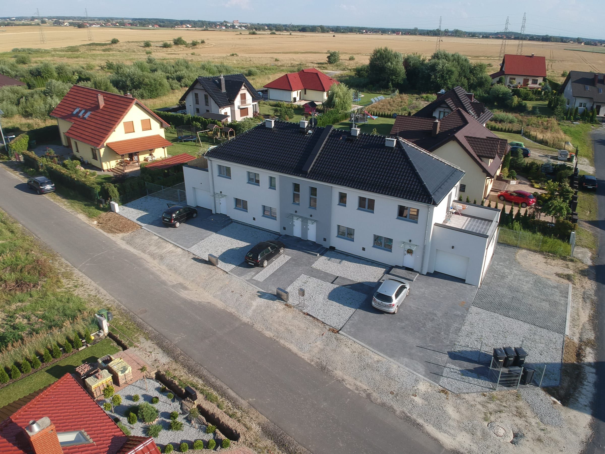 Pogodna z lotu ptaka: biały budynek z grafitowym dachem i garażami, wjazdy z kostki przy osiedlowej ulicy