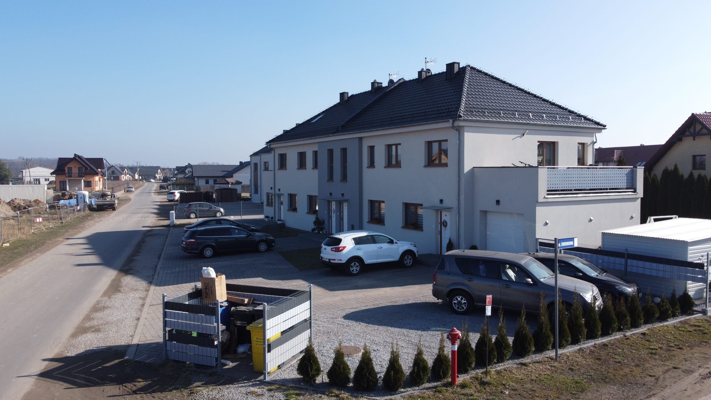 Budynek Poziomkowa 8: biały, dwukondygnacyjny, z dachem czterospadowym, garażem i tarasem, przed nim parking